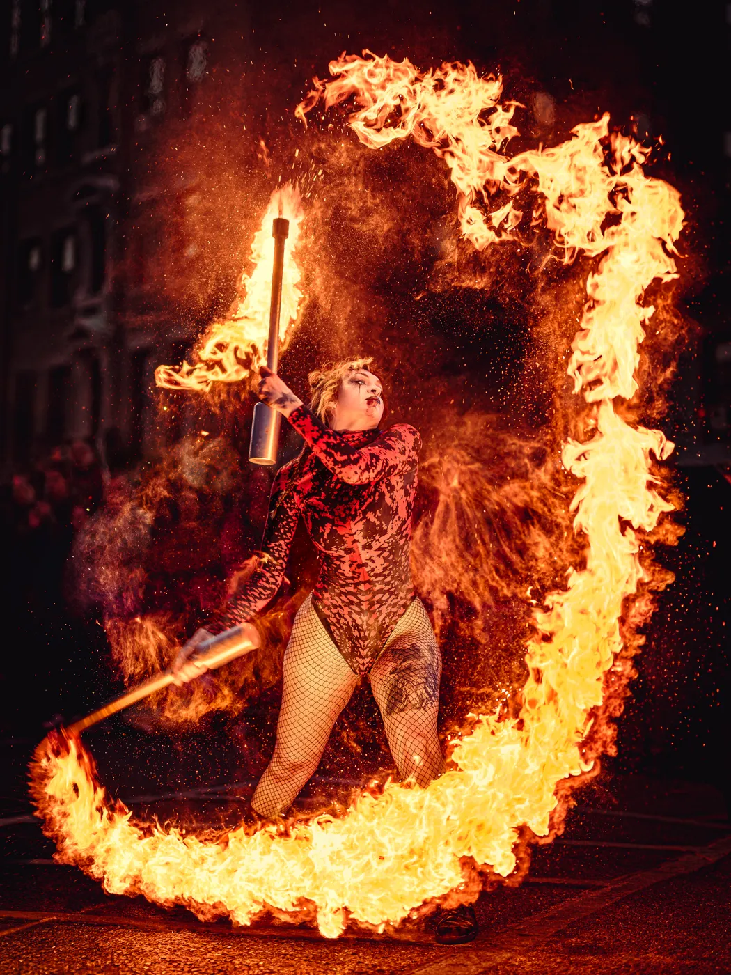 A performer moves a fire staff through a sweeping circle of flame outdoors.