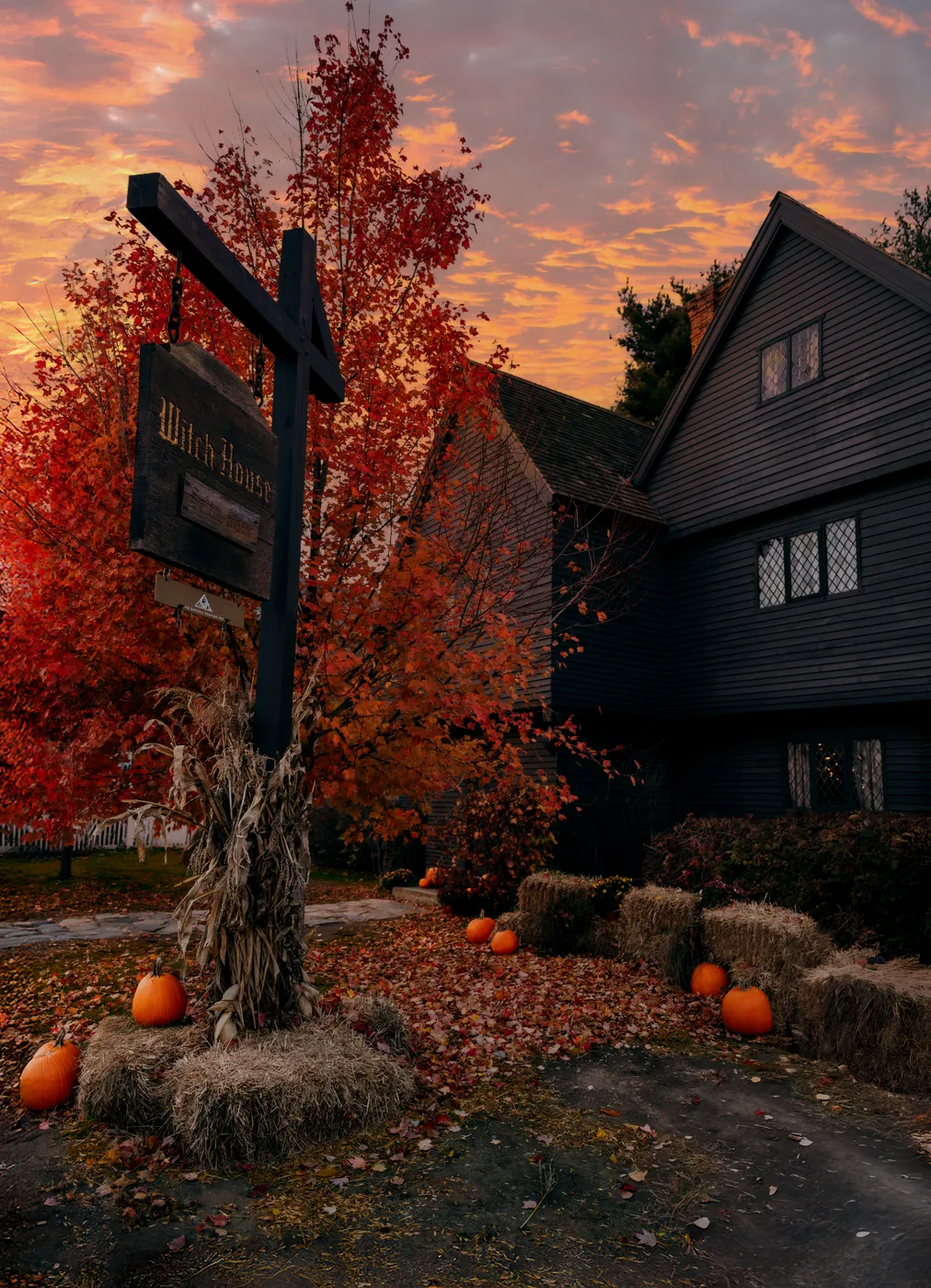 The Witch House sign, dark gables and pumpkins under an orange autumn sky.