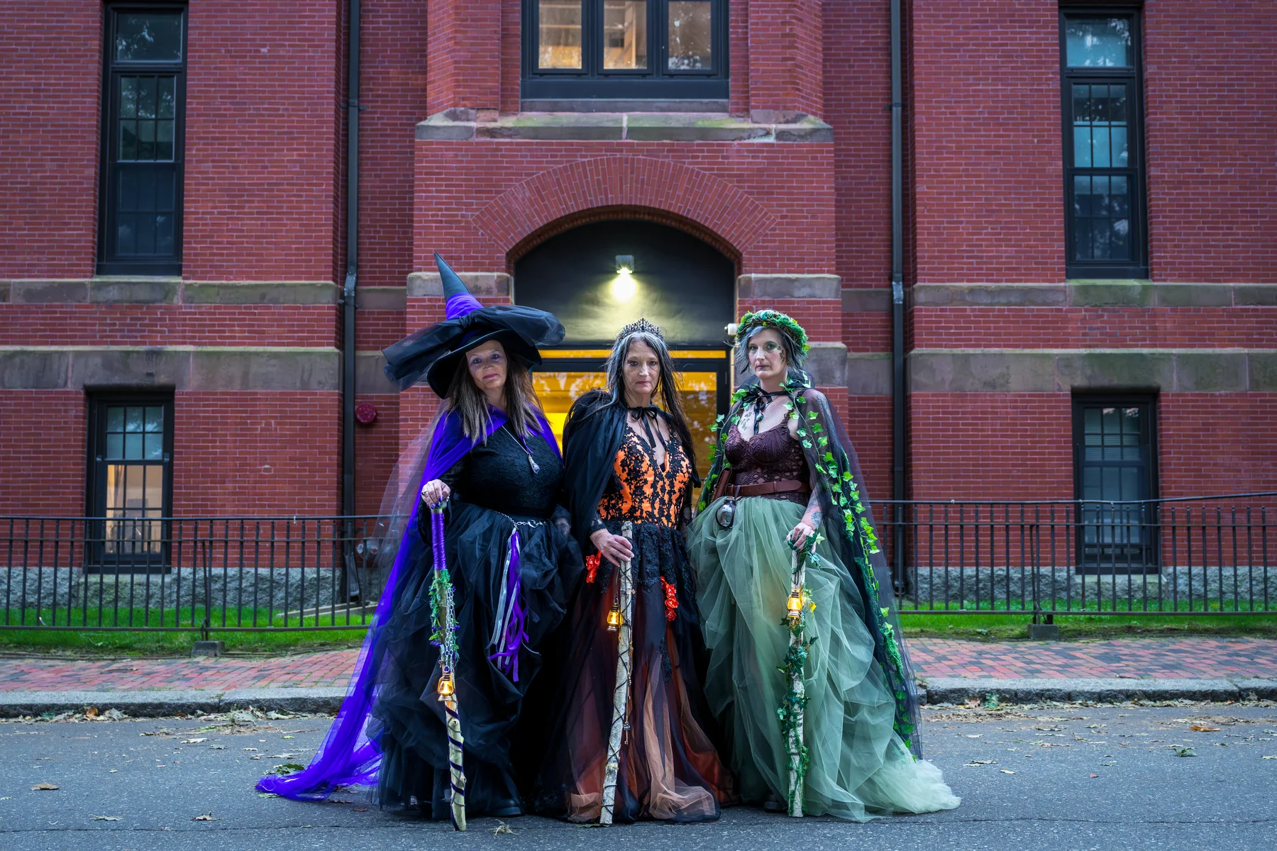 Three costumed women beside a brick building at Salem Common
